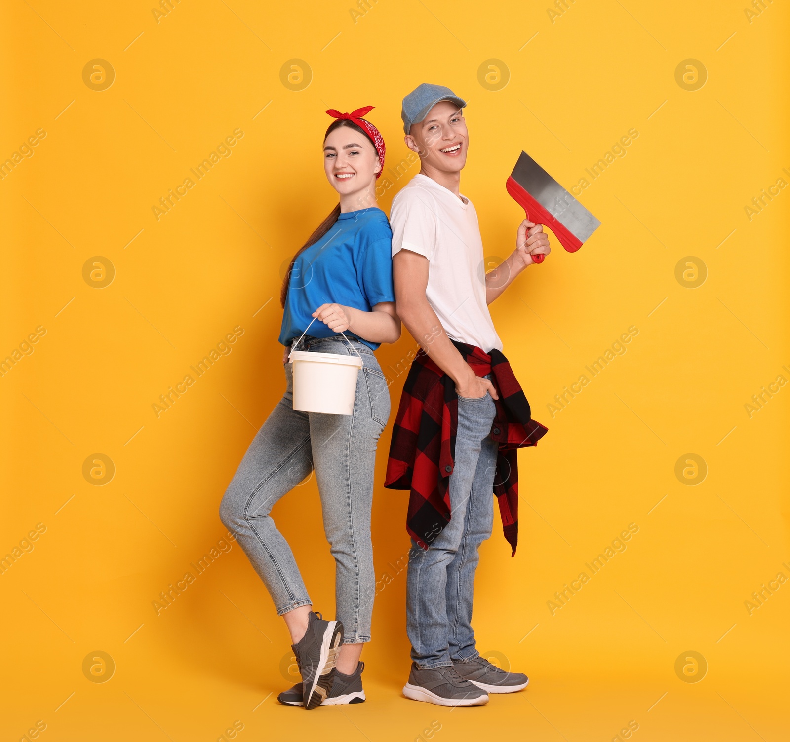 Photo of Professional decorator. Man and woman with different tools on orange background