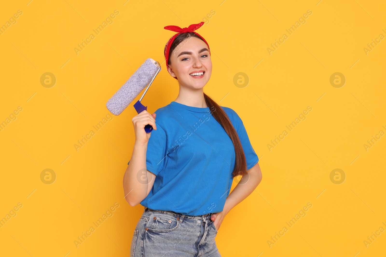 Photo of Portrait of young decorator with paint roller on orange background