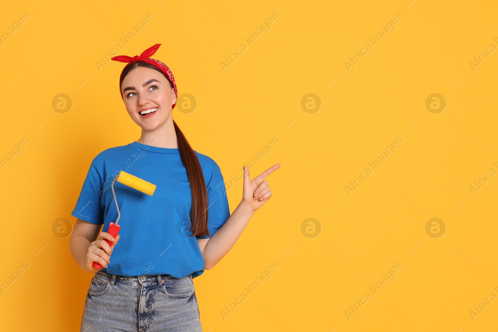 Photo of Portrait of young decorator with paint roller on orange background, space for text