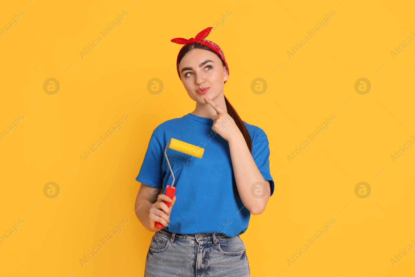 Photo of Portrait of young decorator with paint roller on orange background