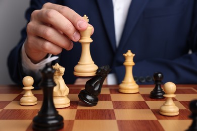 Photo of Businessman playing chess on chessboard against light grey background, closeup. Competition concept