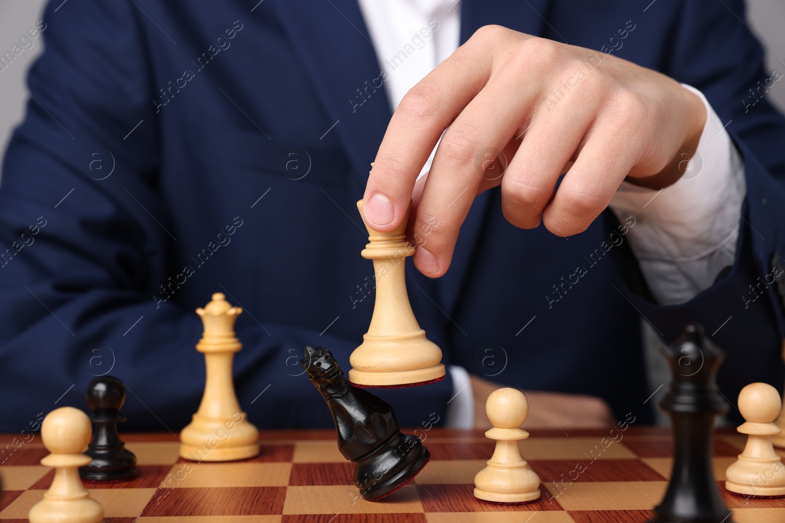 Photo of Businessman playing chess on chessboard against light grey background, closeup. Competition concept