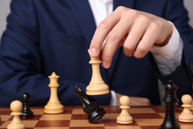 Photo of Businessman playing chess on chessboard against light grey background, closeup. Competition concept