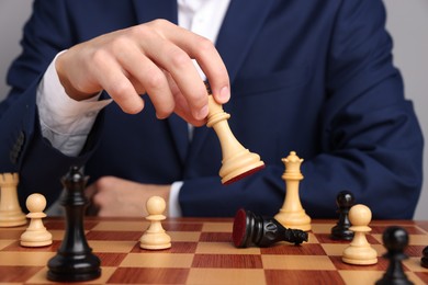 Photo of Businessman playing chess on chessboard against light grey background, closeup. Competition concept