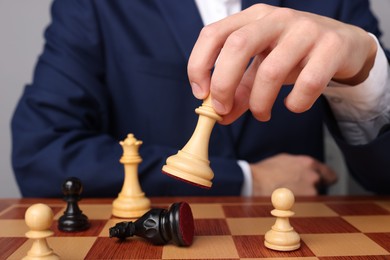 Photo of Businessman playing chess on chessboard against light grey background, closeup. Competition concept