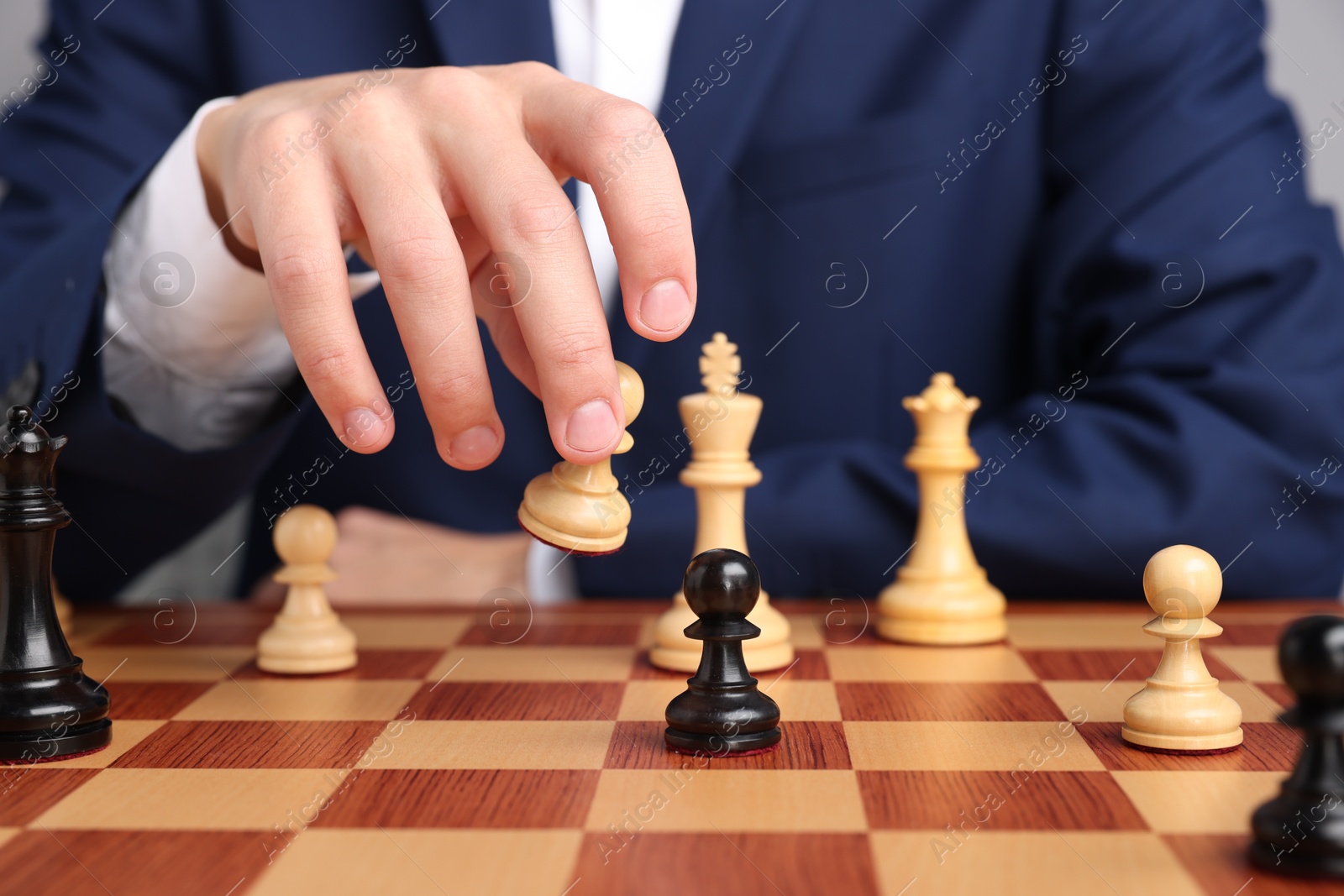 Photo of Businessman playing chess on chessboard against light grey background, closeup. Competition concept