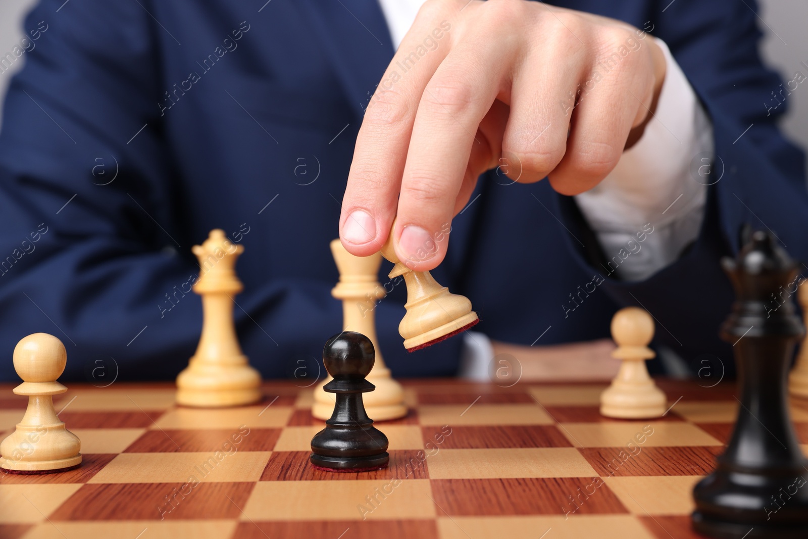 Photo of Businessman playing chess on chessboard against light grey background, closeup. Competition concept