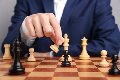 Photo of Businessman playing chess on chessboard against light grey background, closeup. Competition concept