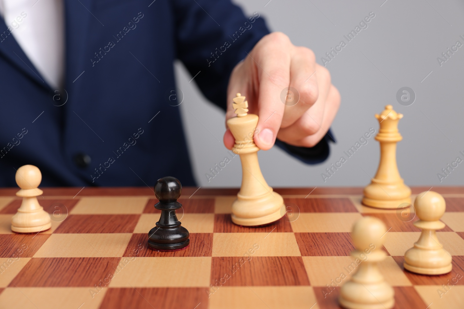 Photo of Businessman playing chess on chessboard against light grey background, closeup. Competition concept