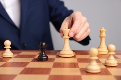 Photo of Businessman playing chess on chessboard against light grey background, closeup. Competition concept