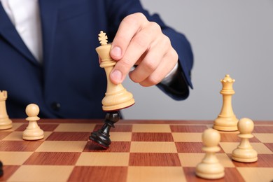 Photo of Businessman playing chess on chessboard against light grey background, closeup. Competition concept