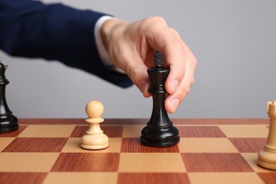 Photo of Businessman playing chess on chessboard against light grey background, closeup. Competition concept