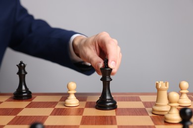 Photo of Businessman playing chess on chessboard against light grey background, closeup. Competition concept