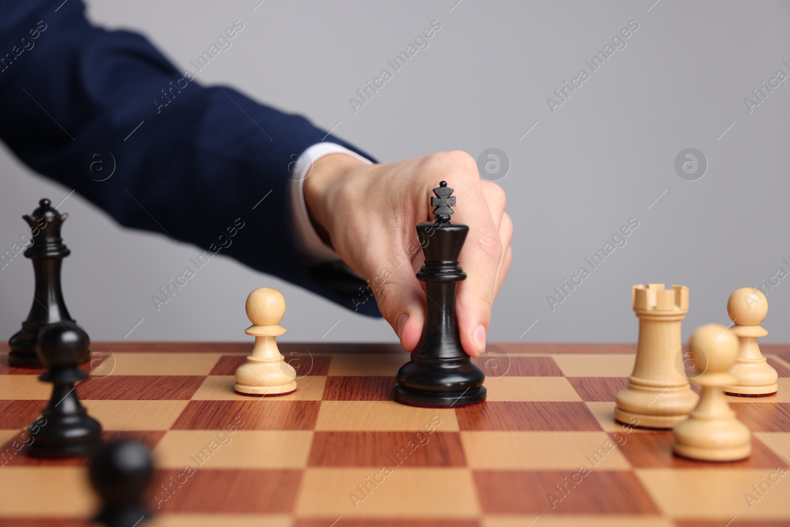 Photo of Businessman playing chess on chessboard against light grey background, closeup. Competition concept