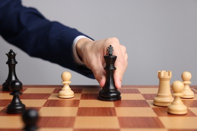 Photo of Businessman playing chess on chessboard against light grey background, closeup. Competition concept