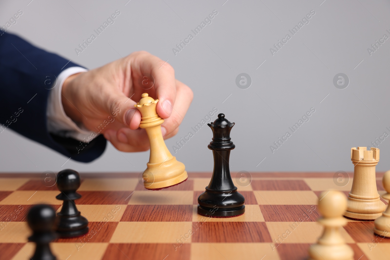 Photo of Businessman playing chess on chessboard against light grey background, closeup. Competition concept