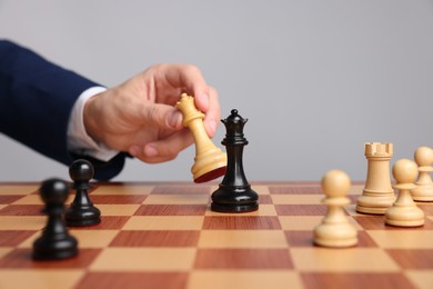 Photo of Businessman playing chess on chessboard against light grey background, closeup. Competition concept