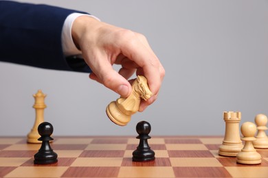 Photo of Businessman playing chess on chessboard against light grey background, closeup. Competition concept