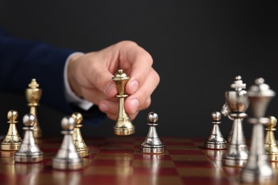 Photo of Businessman playing chess on chessboard against black background, closeup. Competition concept