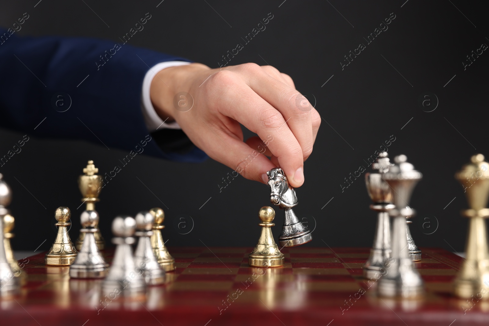 Photo of Businessman playing chess on chessboard against black background, closeup. Competition concept