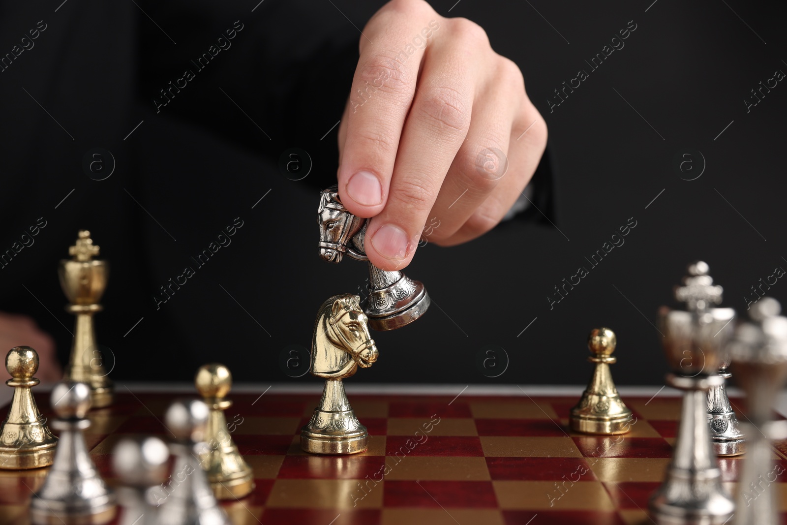 Photo of Businessman playing chess on chessboard against black background, closeup. Competition concept