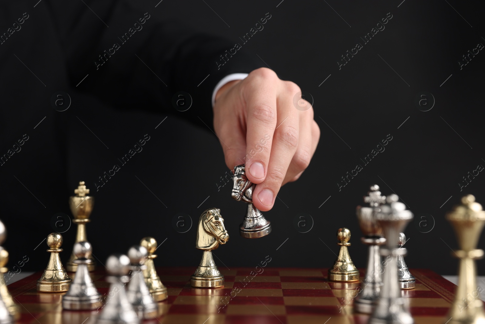 Photo of Businessman playing chess on chessboard against black background, closeup. Competition concept