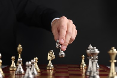 Photo of Businessman playing chess on chessboard against black background, closeup. Competition concept