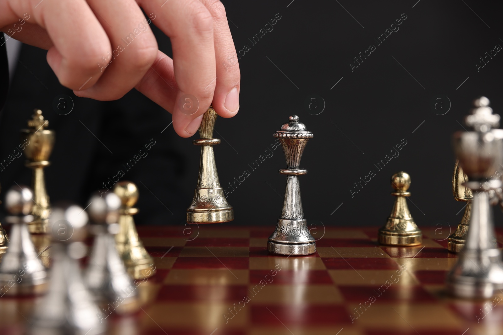 Photo of Businessman playing chess on chessboard against black background, closeup. Competition concept