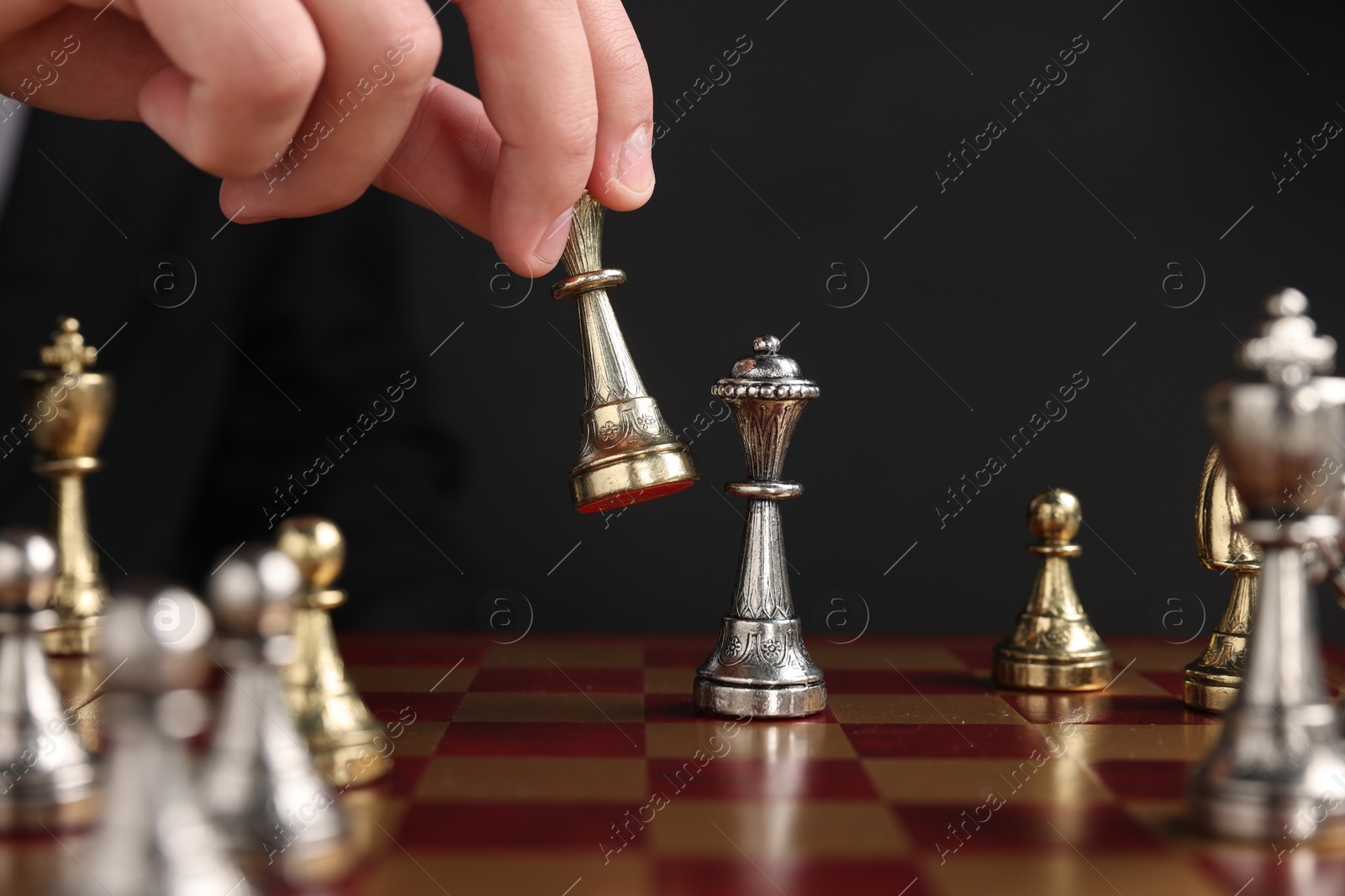 Photo of Businessman playing chess on chessboard against black background, closeup. Competition concept