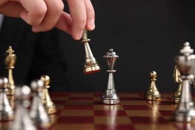 Photo of Businessman playing chess on chessboard against black background, closeup. Competition concept