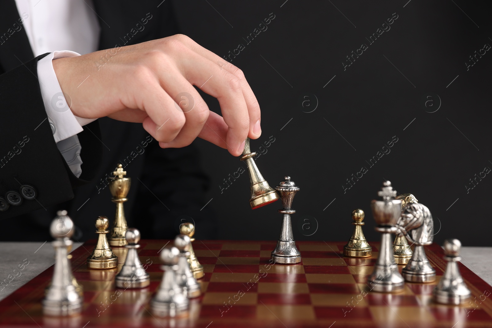 Photo of Businessman playing chess on chessboard against black background, closeup. Competition concept