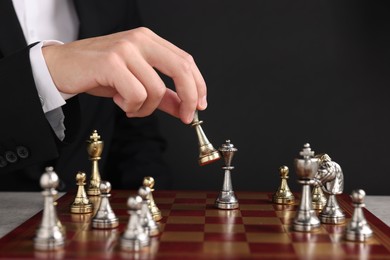 Photo of Businessman playing chess on chessboard against black background, closeup. Competition concept