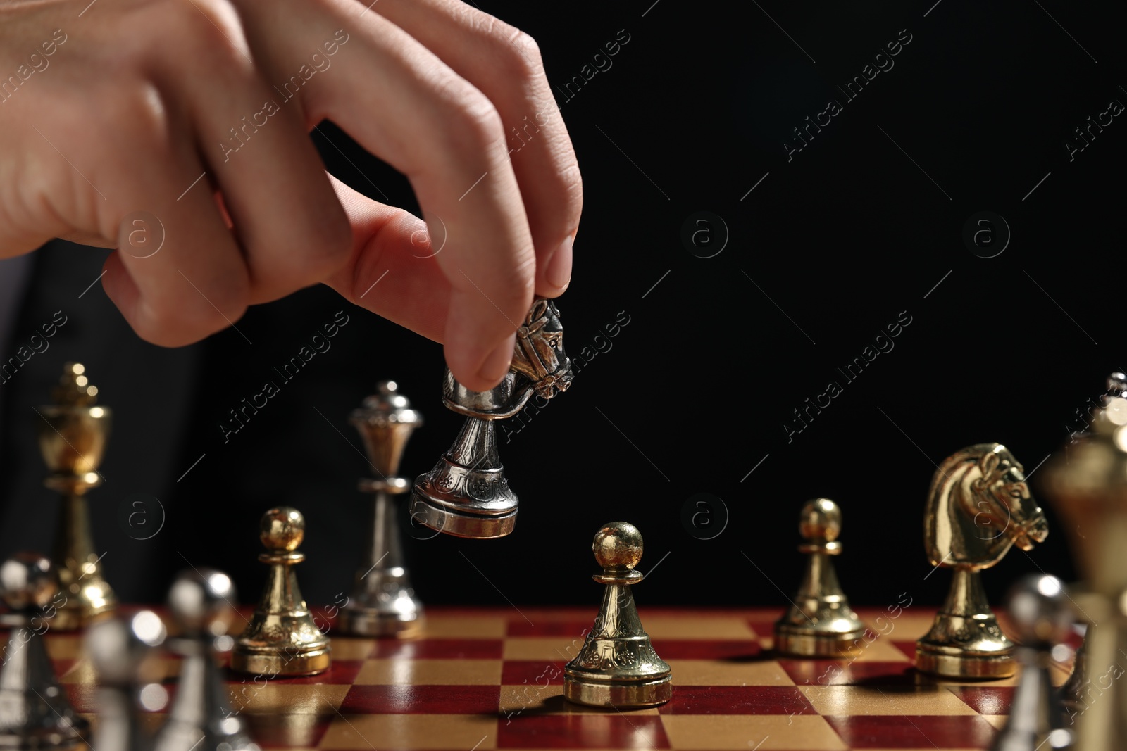 Photo of Businessman playing chess on chessboard against black background, closeup. Competition concept