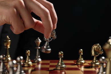 Photo of Businessman playing chess on chessboard against black background, closeup. Competition concept