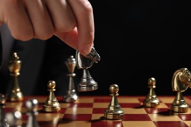 Photo of Businessman playing chess on chessboard against black background, closeup. Competition concept