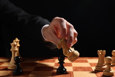 Photo of Businessman playing chess on chessboard against black background, closeup. Competition concept