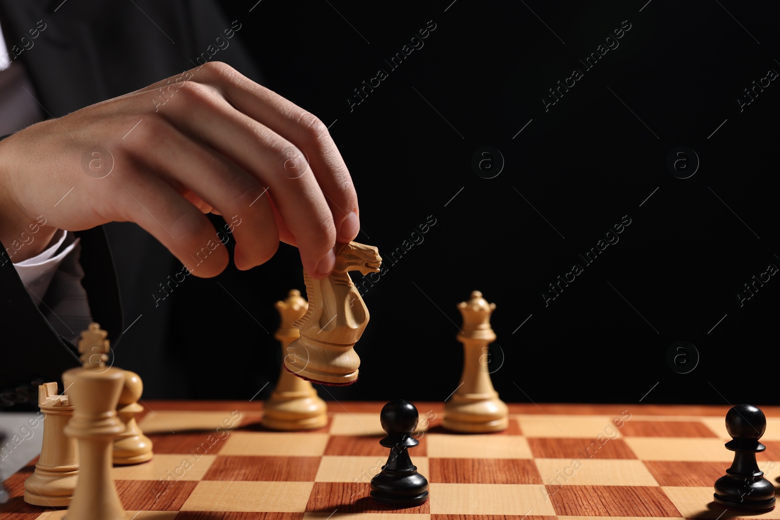 Photo of Businessman playing chess on chessboard against black background, closeup. Competition concept