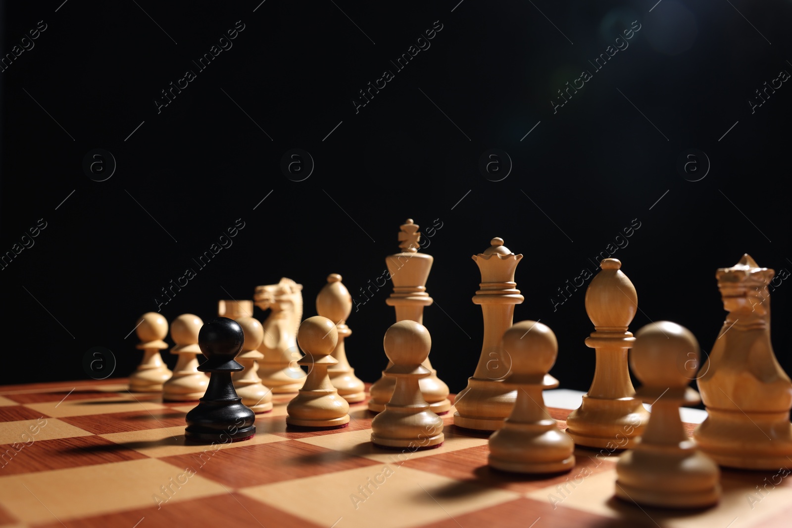 Photo of Black pawn in front of white chess pieces on chessboard, closeup. Competition concept