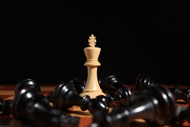 Photo of White chess king among fallen black pieces on chessboard, closeup. Competition concept