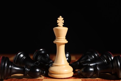 Photo of White chess king among fallen black pieces on chessboard, closeup. Competition concept