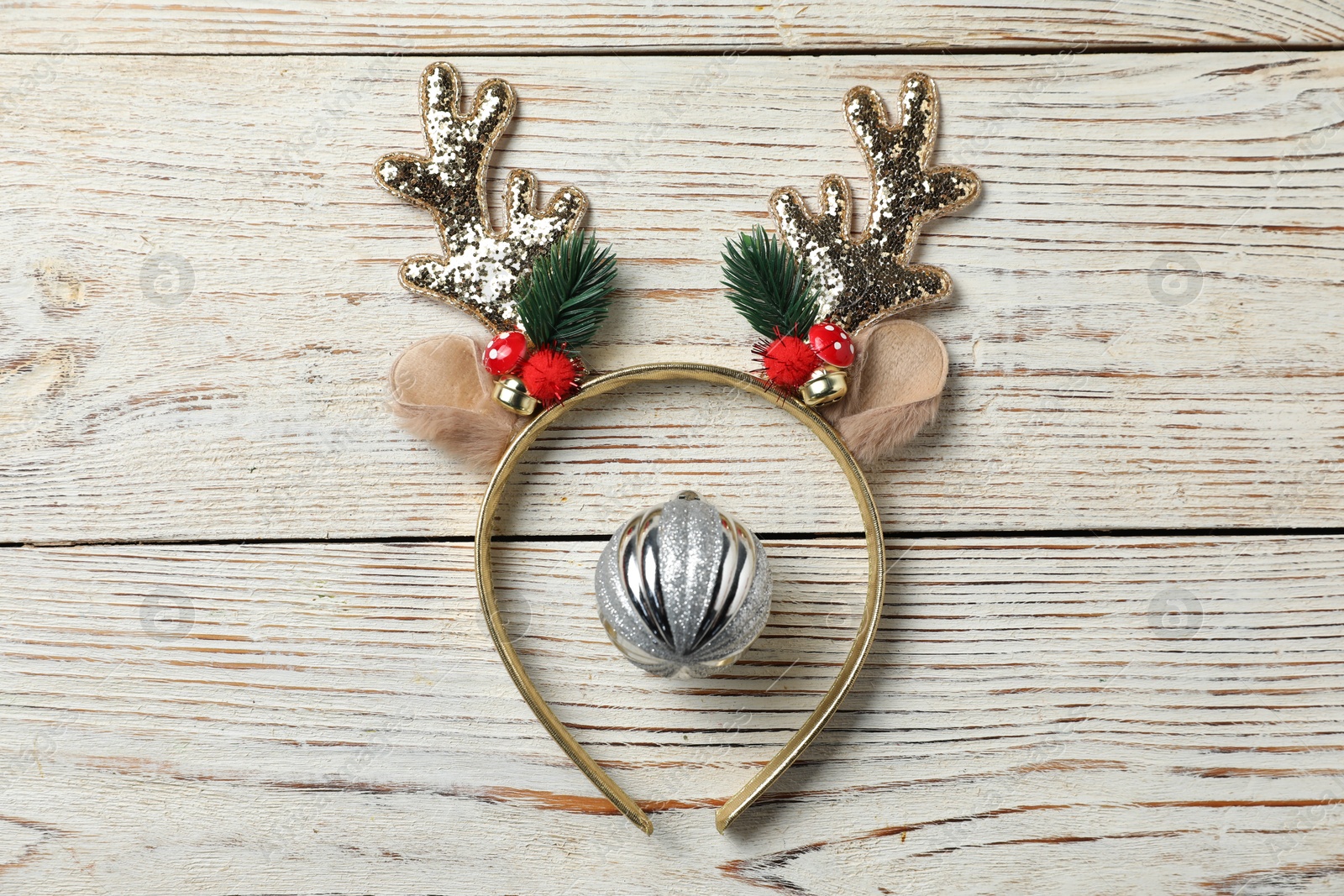 Photo of Beautiful reindeer headband and Christmas bauble on white wooden background, top view