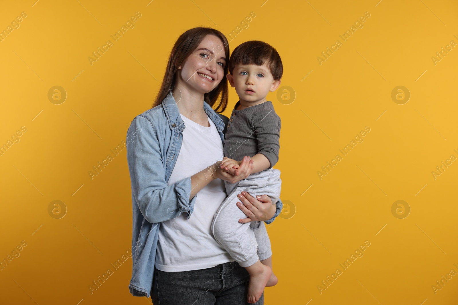 Photo of Happy mother with her cute little son on yellow background, space for text