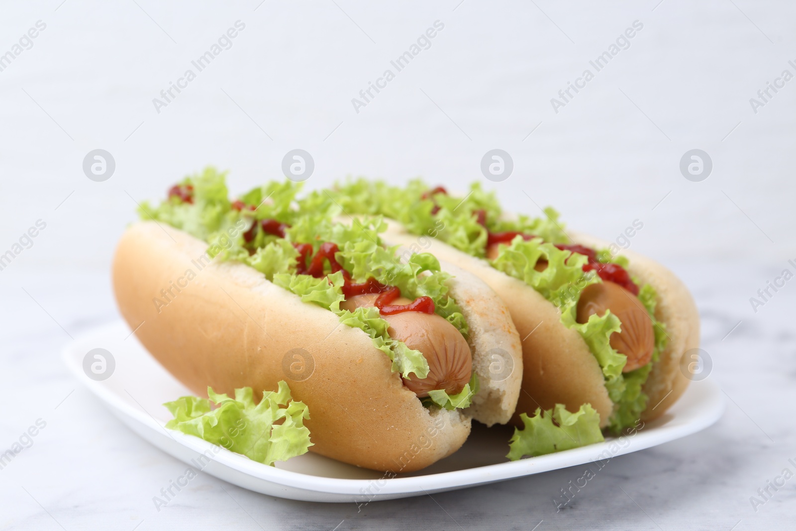 Photo of Tasty hot dogs with lettuce and ketchup on white marble table, closeup