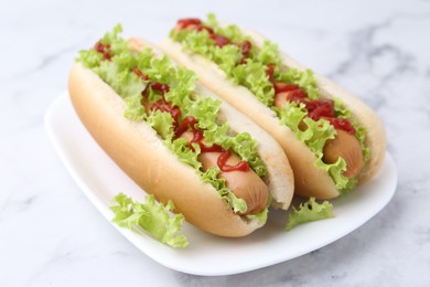 Photo of Tasty hot dogs with lettuce and ketchup on white marble table, closeup