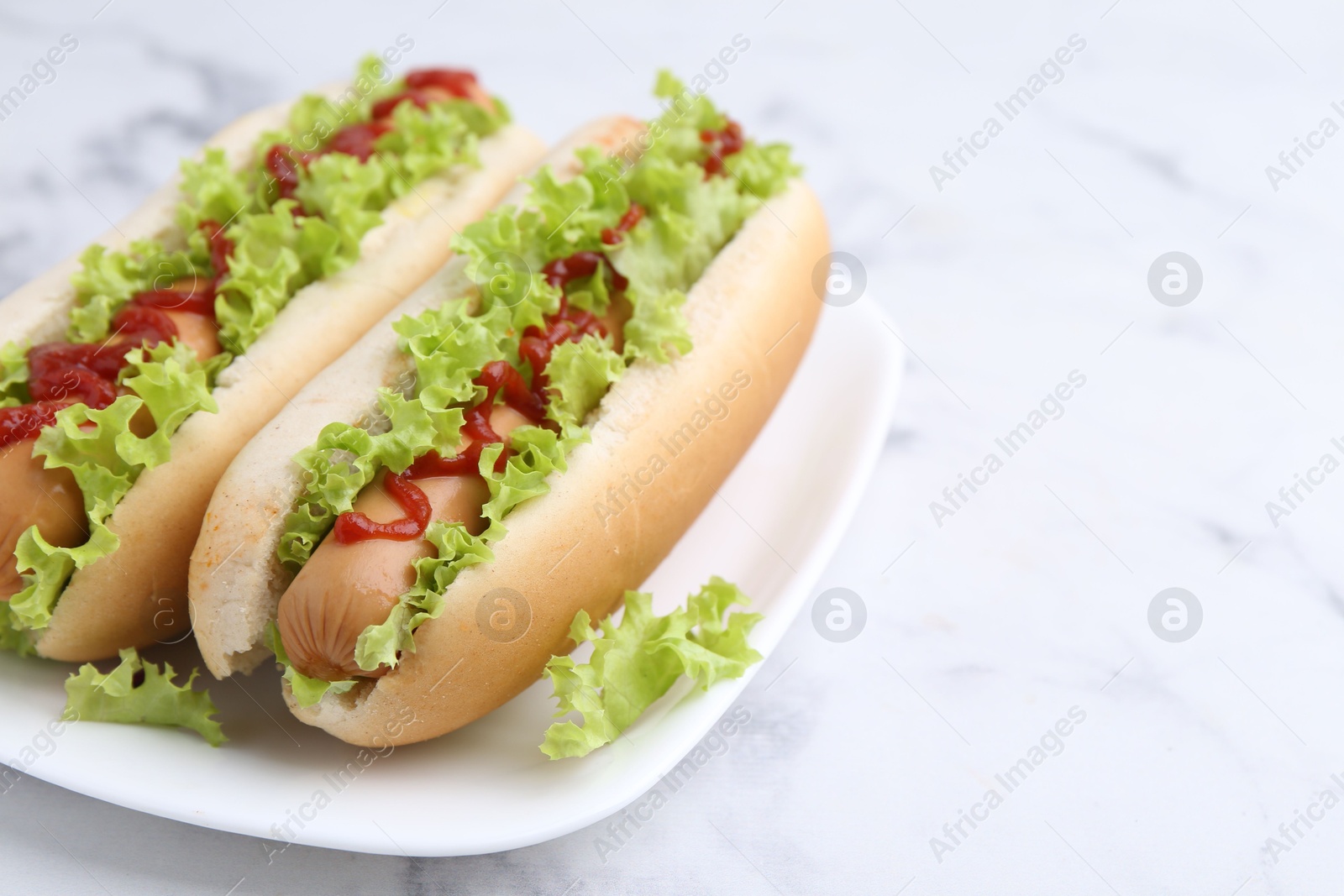 Photo of Tasty hot dogs with lettuce and ketchup on white marble table, closeup. Space for text