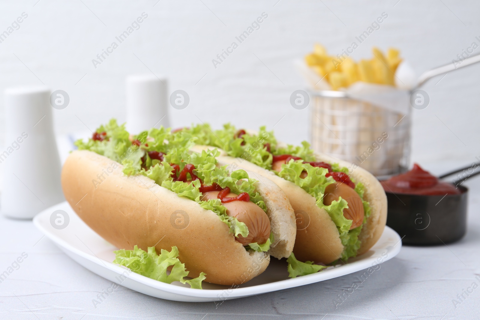 Photo of Tasty hot dogs with lettuce and ketchup on white table, closeup