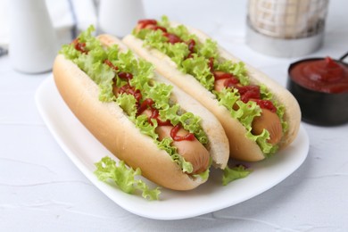 Photo of Tasty hot dogs with lettuce and ketchup on white table, closeup