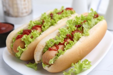 Photo of Tasty hot dogs with lettuce and ketchup on white table, closeup