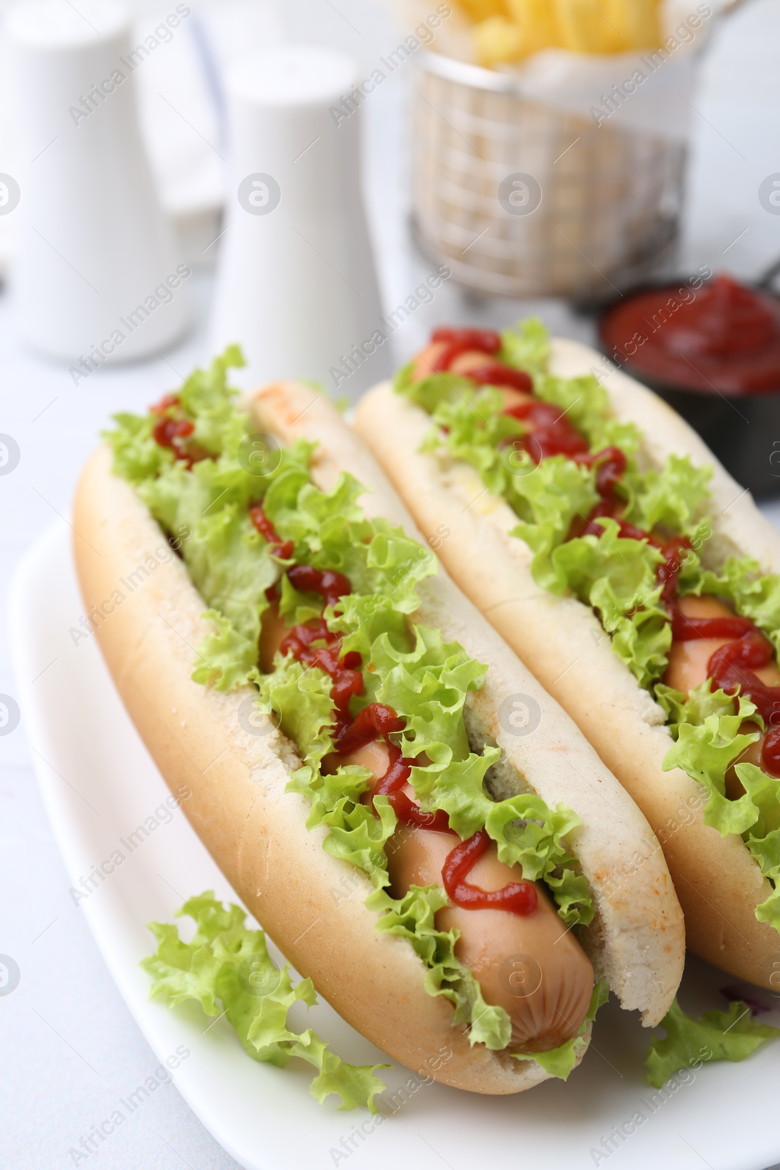 Photo of Tasty hot dogs with lettuce and ketchup on white table, closeup