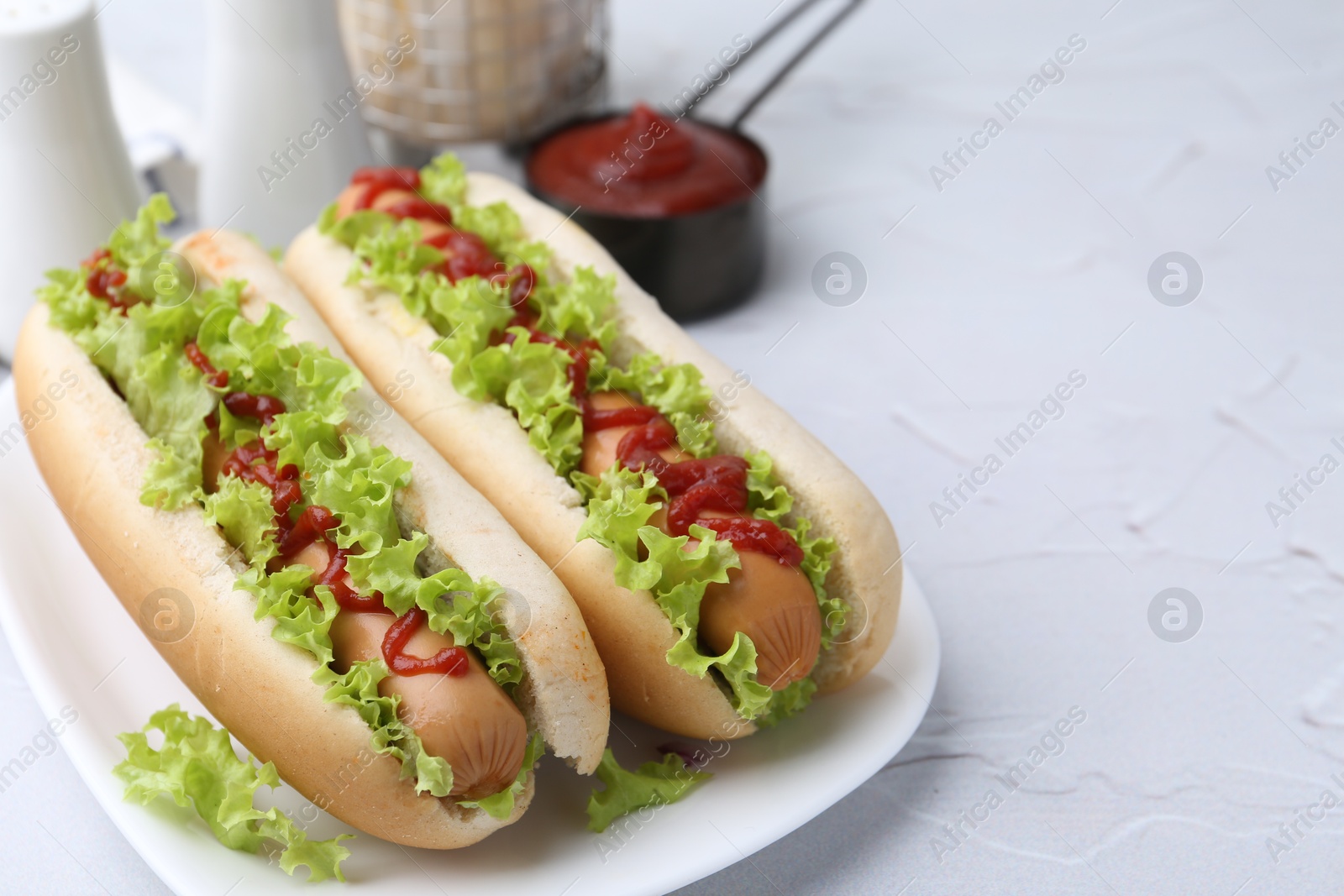 Photo of Tasty hot dogs with lettuce and ketchup on white table, closeup. Space for text